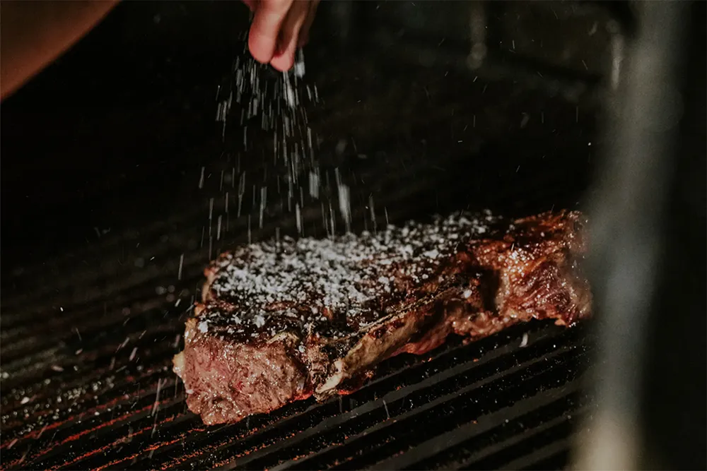 Txuleta de vacuno a la parrilla mientras se añade sal gruesa durante su preparación en Asador Nicolás de Tolosa.