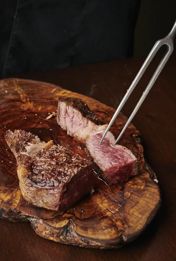 Txuleta de vacuno mayor a la parrilla, cortada sobre una tabla de madera y servida al punto en Asador Nicolás.
